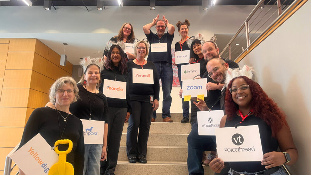 A group of people posing on stairs holding signs that list the names of various learning technologies